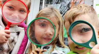Drei Kinder halten sich jeweils eine Lupe vor das Gesicht