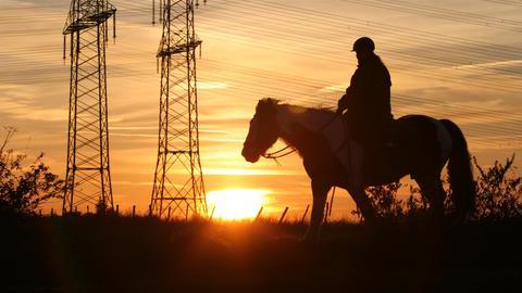 Eine Person reitet im Sonnenuntergang auf einem Pferd.