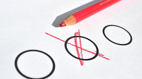 Ein roter Stift, der auf einem Papier liegt, auf dem drei Kreise zu sehen sind. Ein Kreis wurde mit einem Kreuz markiert.