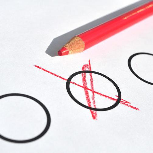 Ein roter Stift, der auf einem Papier liegt, auf dem drei Kreise zu sehen sind. Ein Kreis wurde mit einem Kreuz markiert.