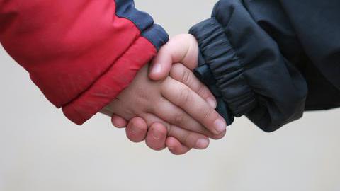 Zwei Kinder halten sich an den Hände (im Bildausschnitt sind nur die Hände zu sehen)