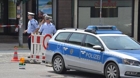 Zwei Polizisten und ein Polizeifahrzeug, mit dem eine Straße gesperrt wird.