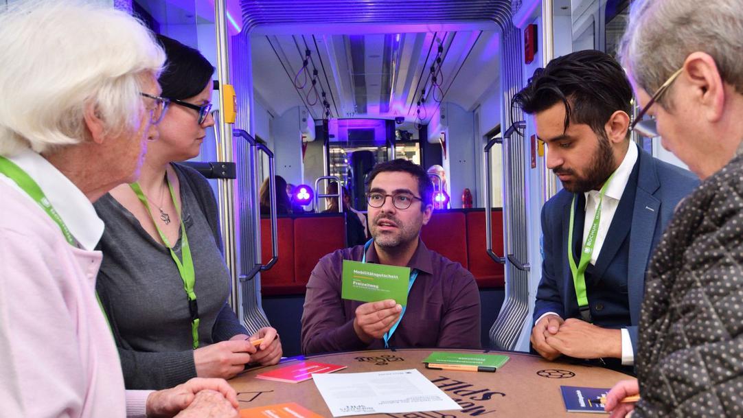 Ein Bild von der Bürgerkonferenz 2019, wo Menschen im Kreis in einer Straßenbahn sitzen