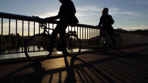 Radfahrer genießen  während des Sonnenuntergangs auf einer Brücke über dem Fluss Ruhr in Bochum-Stiepel die Aussicht.