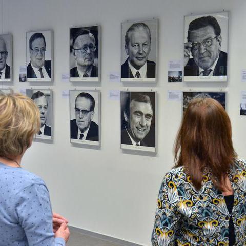Eröffnung einer Ausstellung im Stadtarchiv - zwei Besucherinnen betrachten Porträtbilder an einer Wand.