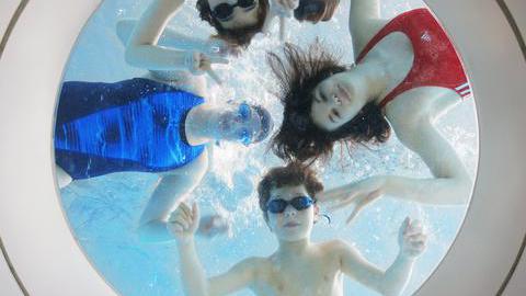 Vier Kinder im Schwimmbad schauen durch ein Fenster