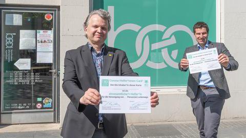 Geschäftsführer Uwe van der Lely und Oberbürgermeister Thomas Eiskirch halten am 27.04.2020 vor der Tür zur Bochumer Ehrenamtsagentur eine vergrößerte Darstellung der "Corona-HelferInnen-Card" in den Händen