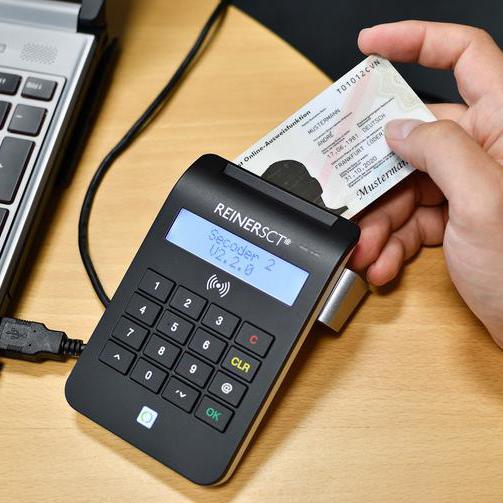 Illustration zum neuen Bürgerserviceportal: Ein elektronischer Personalausweis wird neben einem Laptop in ein Lesegerät gesteckt.