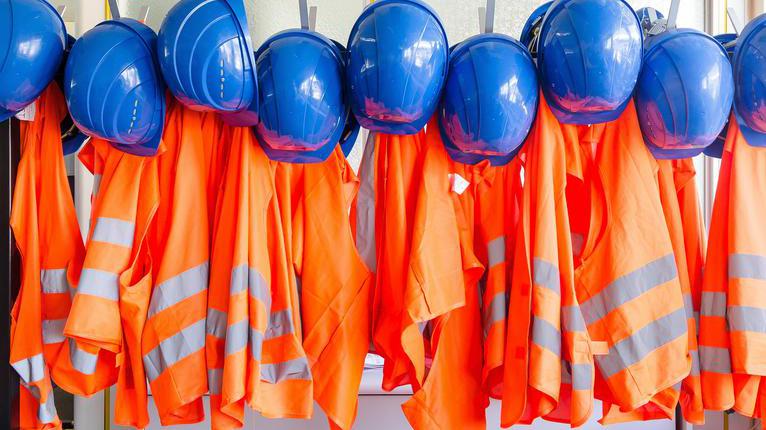 Helme und Warnwesten hängen an einer Garderobe.