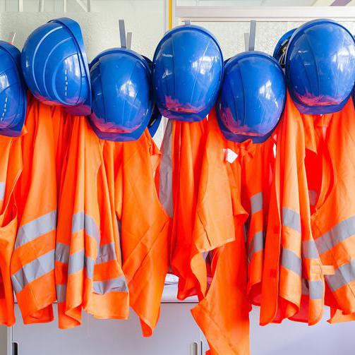 Helme und Warnwesten hängen an einer Garderobe.