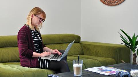 Symbolfoto eGovernment - Eine Frau sitzt auf einem Sofa und hat einen Laptop auf den Knien.