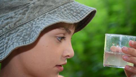 Ein Junge untersucht in einem Gefäß eine Wasserprobe