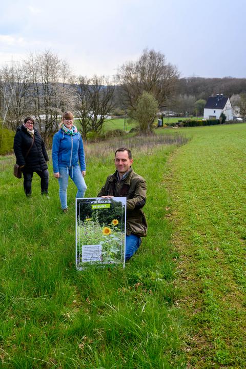 Kooperationspartner, Landwirt Jan Bockholt auf einer Wiese stehend, mit einem Plakat des Projekts - ökologische Aufwertung landwirtschaftlicher Flächen.