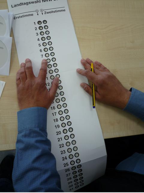 Ein Mann füllt einen Wahlzettel mit einem Bleistift aus.