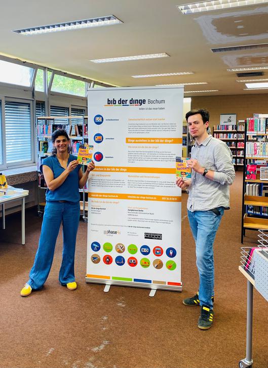 Mitarbeiter vor einem Plakat der Bibliothek der Dinge
