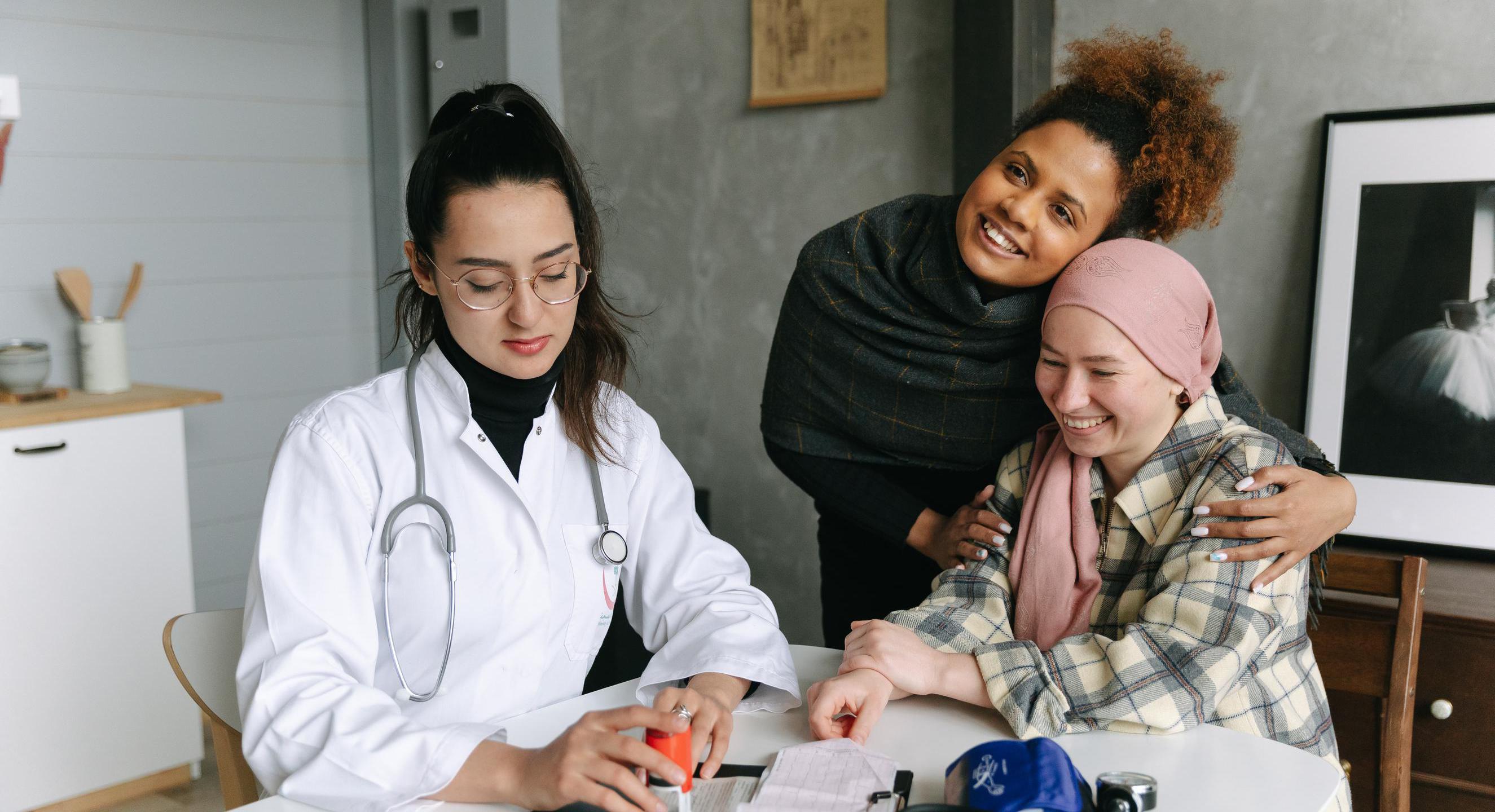 Eine Ärztin sitzt am Tisch in einem Beratungsgespräch mit zwei Patientinnen. Auf dem Tisch liegt ein Blutdruckmessgerät. Alle Frauen lächeln.