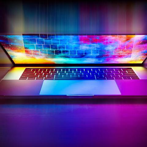 Ein halb aufgeklappte Laptop, auf dessen Bildschirm ein bunter Desktop zu sehen ist, dessen Farben gelb, grün, blau und lila das gesamte Bild erhellen.