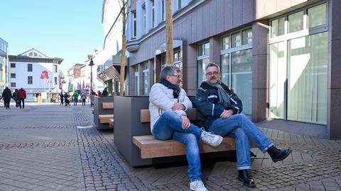Bezirksbürgermeister Hans-Peter Herzog und Baudezernent Dr. Markus Bradtke sitzen auf einer Bank vor mobilen Bäumen in Bochum-Wattenscheid.