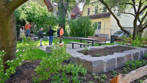 Das Bild zeigt eine kleine Grünanlage, einen sogenannten Pocket Park, mit Sitzmöglichkeit und Kräuterbeeten. In der Mitte wird ein Mitarbeiter der Stadt Bochum zum Pocket Park interviewt.