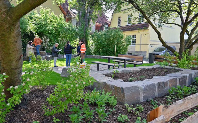 Das Bild zeigt eine kleine Grünanlage, einen sogenannten Pocket Park, mit Sitzmöglichkeit und Kräuterbeeten. In der Mitte wird ein Mitarbeiter der Stadt Bochum zum Pocket Park interviewt.
