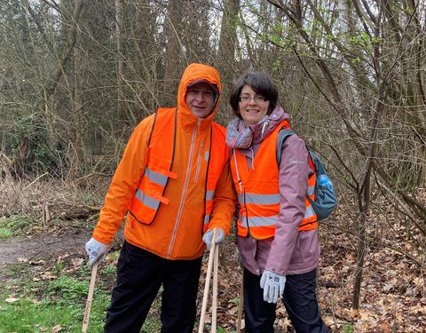 Ein Ehepaar (links der Mann, rechts die Frau) posiert gemeinsam mit orangefarbenen Westen für das Foto.