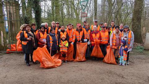 Eine Gruppe aus ca. 25 Personen posieren mit ihren orangenen Müllsäcken für das Foto.