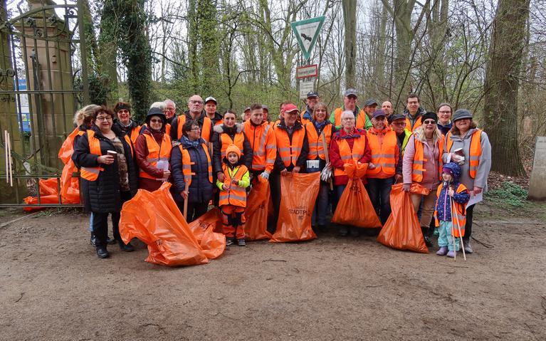 Eine Gruppe aus ca. 25 Personen posieren mit ihren orangenen Müllsäcken für das Foto.