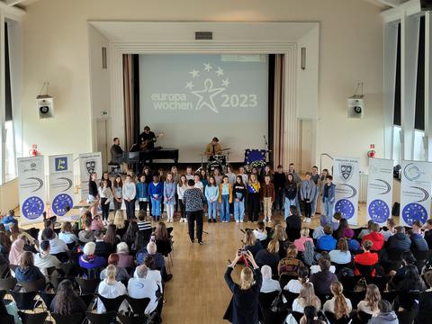 Menschen in einer Aula mitsamt Kindern, die singen