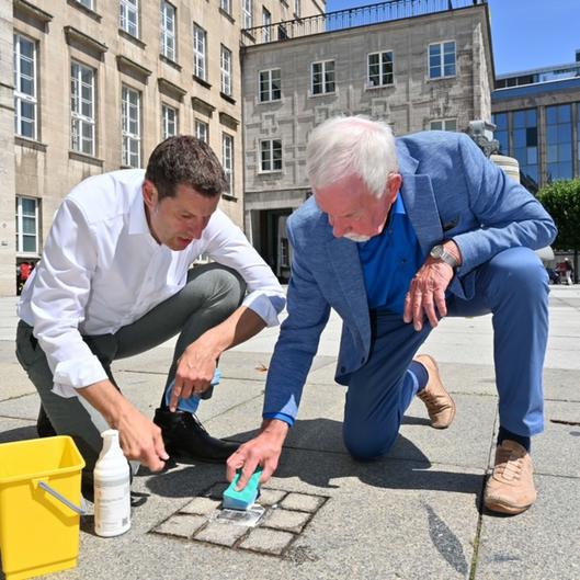 Thomas Eiskirch und  Ernst-Otto Stüber reinigen den Stolperstein für Dr. Otto Ruer 