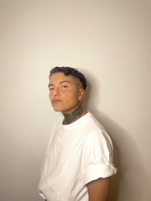 Das Bild zeigt einen Mann mit kurzen dunklen Haaren und Tattoos zwischen 20 und 30 Jahren. Er trägt ein weißes T-Shirt und ist von der Seite zu sehen. Es ist der DJ Nury.