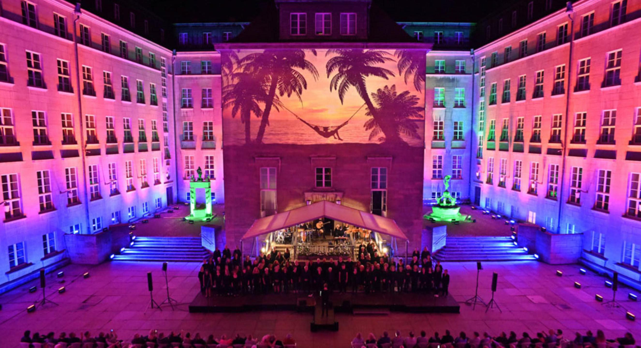 Das Bild zeigt den Innenhof des Rathaus in Bochum während eines Konzertes. Ein Strandbild wird auf die Hauswand projeziert.