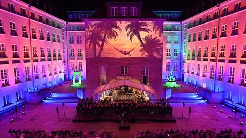 Das Bild zeigt den Innenhof des Rathaus in Bochum während eines Konzertes. Ein Strandbild wird auf die Hauswand projeziert.