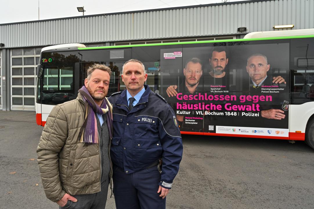 Schauspieler Roland Riebeling und Polizist Andreas Derks stehen vor einem Bus mit dem Motiv einer Kampagne gegen häusliche Gewalt, für das sie gemeinsam mit VfL-Sportchef Patrick Fabian fotografiert wurden.