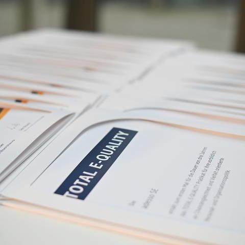 Dokumentenmappen, die Urkunden des Total-E-Quality-Awards beinhalten, auf einem Tisch