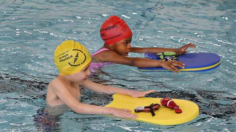 Zwei jungen, die mit Schwimmbrett im Wasser Schwimmen lernen.