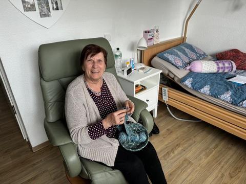 Eine 80jährige Frau sitzt in einem grünen Sessel und strickt.