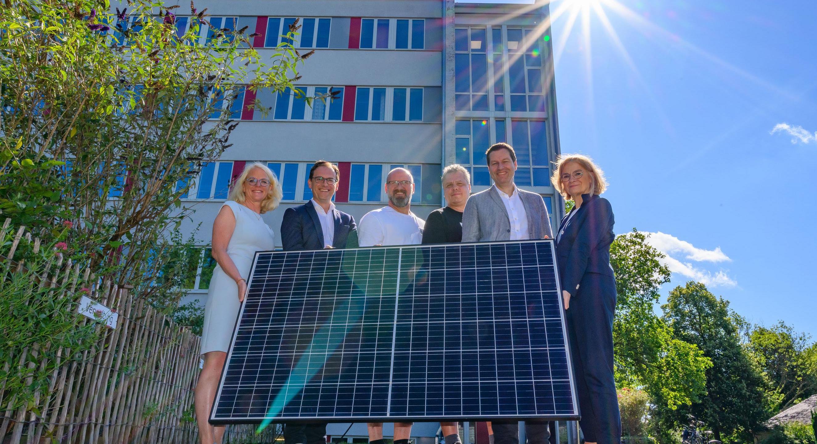 Oberbürgermeister Thomas Eiskirch und Mitarbeitende der Stadt Bochum halten eine Solar-Fläche, die durch Sonne Strom erzeugt.