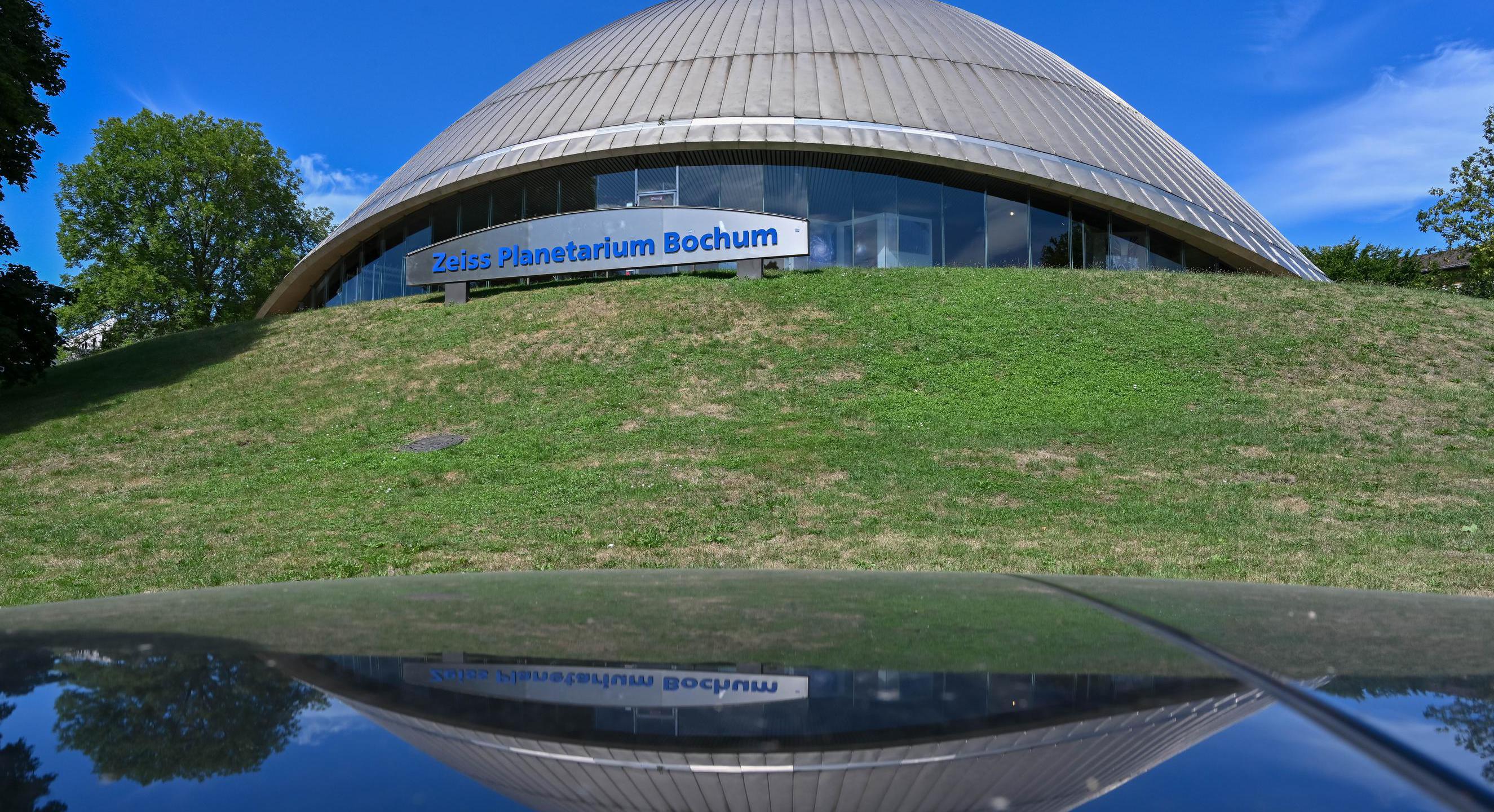Das Bild zeigt die Kuppel des Planetariums von außen vor einer grünen Wiese.