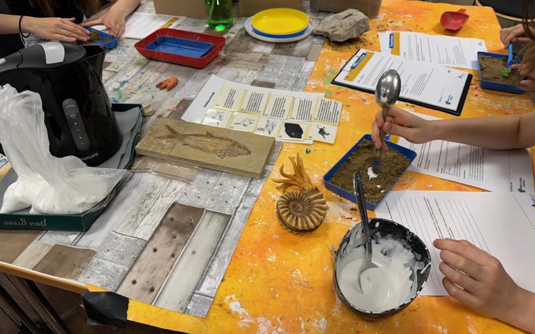 Ein gelber Arbeitstisch von oben, darauf Sand und Formen, um Fossilien selbst zu machen.