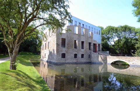 Modernes Gebäude in alten Steinruinen, umgeben von Grün und Wasser.