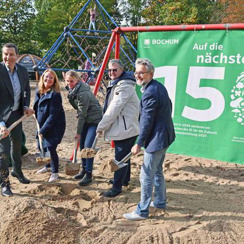 Fünf Personen stehen mit Schaufeln beim Spatenstich im Stadtpark vor einem grünen Banner.
