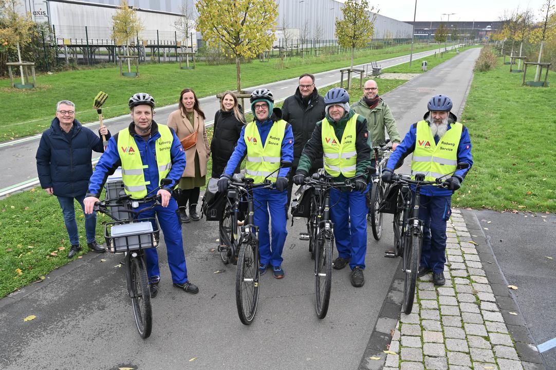 Gruppe von neun Menschen, vier von ihnen haben Warnwesten an und Fahrräder neben sich.