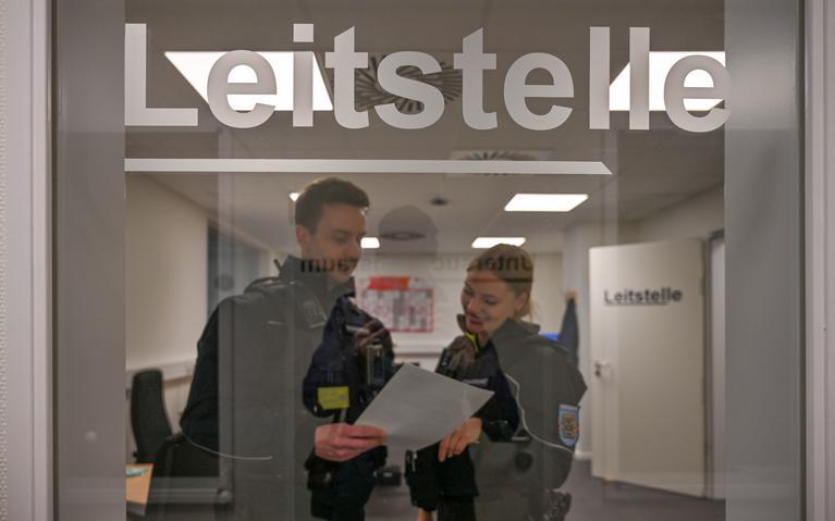 Zwei Mitarbeiter der Citywache stehen in Uniform hinter einer Glastür.
