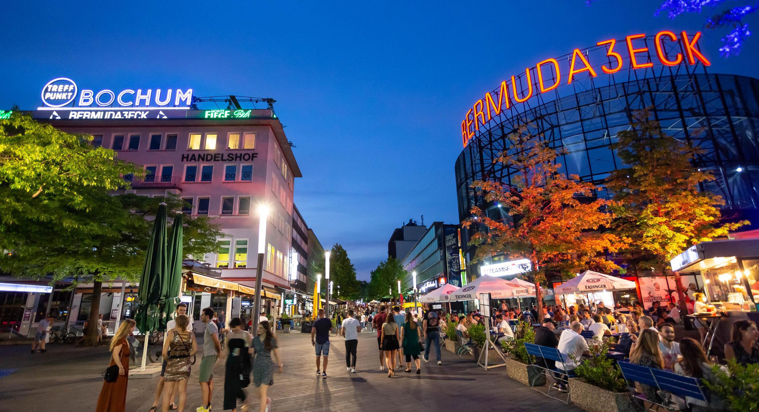 Menschen sitzen oder stehen in der Kneipenstraße.