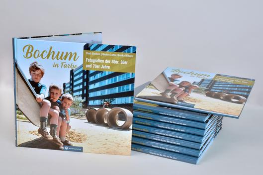 Der Umschlag des Bildbandes "Bochum in Farbe" ist zu sehen und mehrere Exemplare des Buches liegen gestapelt auf dem Tisch.