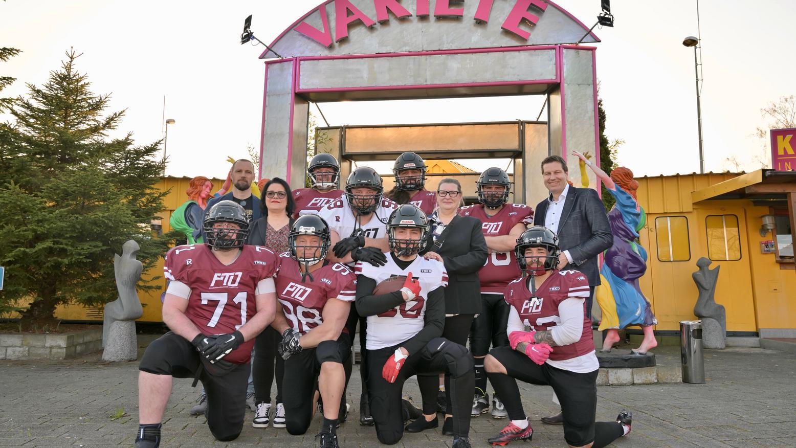American Football-Mannschaft zusammen mit Oberbürgermeister Thomas Eiskirch vor dem dem Eingang zum Varieté „et cetera“