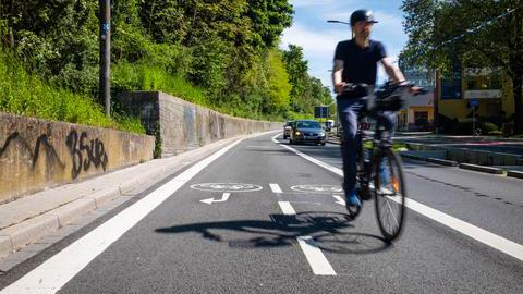 Ein Mann auf einem Fahrrad auf einem neuen Fahrradweg an einer Straße. 