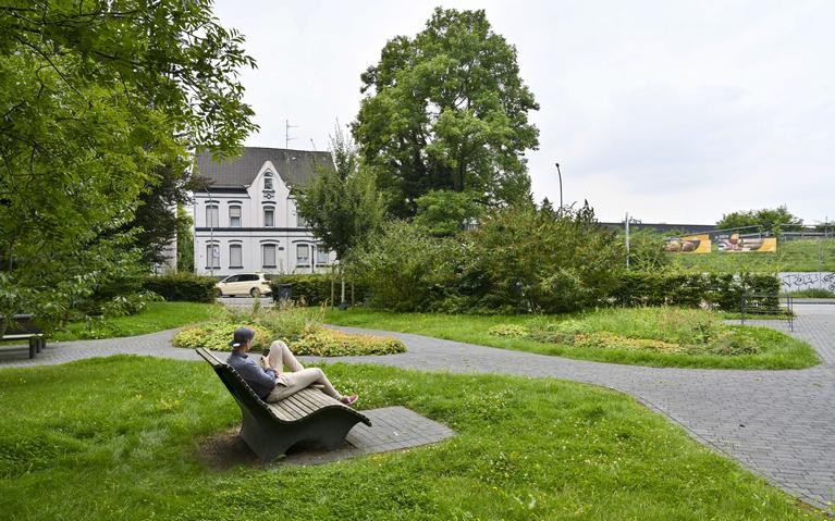 Eine Bank in einem kleinen Park, auf der ein junger Mann sitzt.