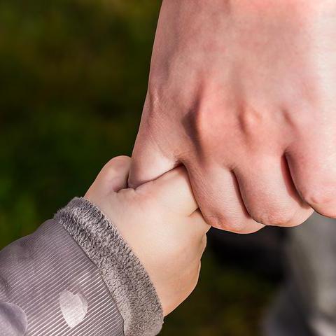 Eine Kinderhand hält sich an der Hand eines Erwachsenen fest.