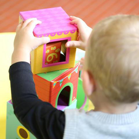 Man sieht den Rücken eines Kindes. Es baut einen Turm aus Stapelsteinen.